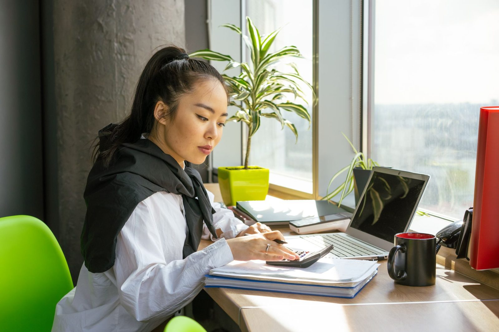 Business professional calculating expenses beside a laptop.